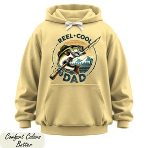 A yellow hoodie with a graphic design featuring a fish and the text "REEL. COOL. DAD" printed on it.