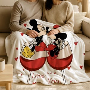 A couple sitting on a couch, wrapped in a blanket featuring a cartoon image of Mickey Mouse and Minnie Mouse.