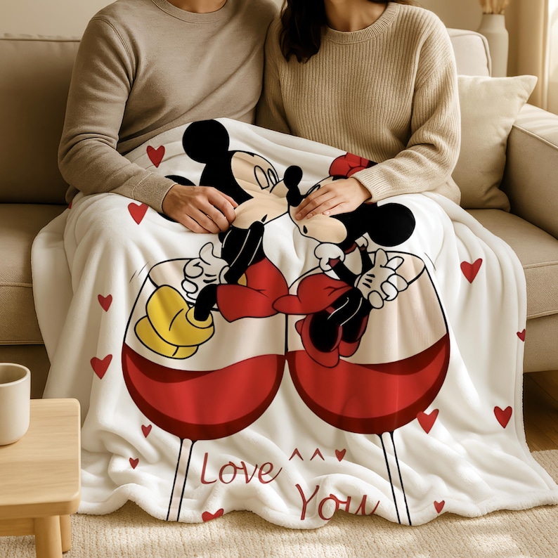 A couple sitting on a couch, wrapped in a blanket featuring a cartoon image of Mickey Mouse and Minnie Mouse.