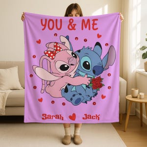 A person holding up a pink blanket with a cartoon image of two characters, one pink and one blue, along with the text "YOU & ME" and the names "Sarah" and "Jack".