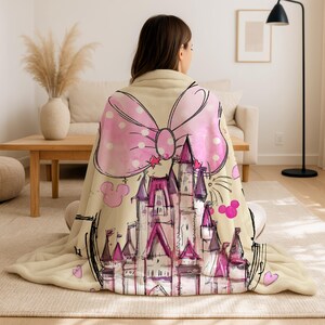 A woman sitting on the floor with a pink and white polka dot blanket featuring a castle design.