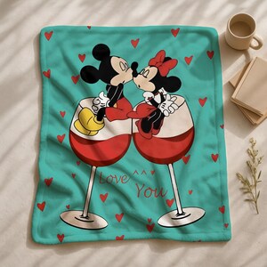 A blanket with a cartoon image of Mickey Mouse and Minnie Mouse sitting together in wine glasses, surrounded by red hearts, with the text "Love You" written on it.