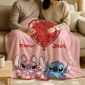 A couple sitting on a couch, wrapped in a pink blanket featuring the characters Stitch and Amber from the movie Lilo & Stitch.