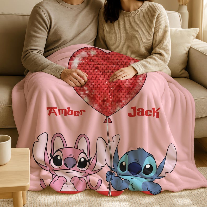 A couple sitting on a couch, wrapped in a pink blanket featuring the characters Stitch and Amber from the movie Lilo & Stitch.