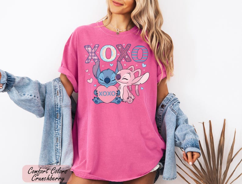 A woman wearing a pink t-shirt with a cartoon character and the text "XOXO" is posing in front of a plant.