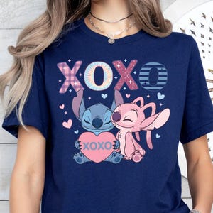 A woman wearing a navy blue t-shirt with a graphic design featuring two cartoon characters, a pink one and a blue one, along with the text "XOXO" and hearts.
