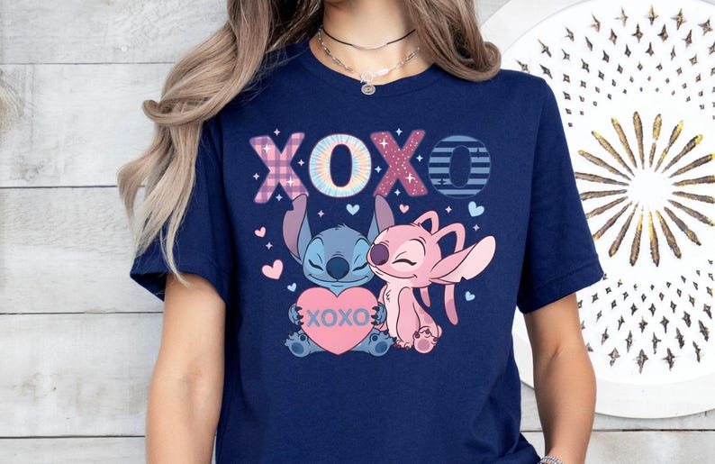 A woman wearing a navy blue t-shirt with a graphic design featuring two cartoon characters, a pink one and a blue one, along with the text "XOXO" and hearts.