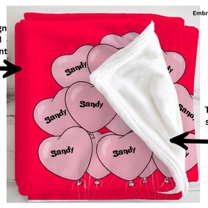 a red blanket with a white towel partially covering it, along with a series of pink heart-shaped balloons with the word "Sandy" printed on them.