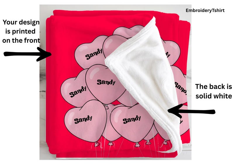 a red blanket with a white towel partially covering it, along with a series of pink heart-shaped balloons with the word "Sandy" printed on them.