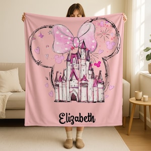 A woman is holding up a pink blanket with a castle and a bow on it.