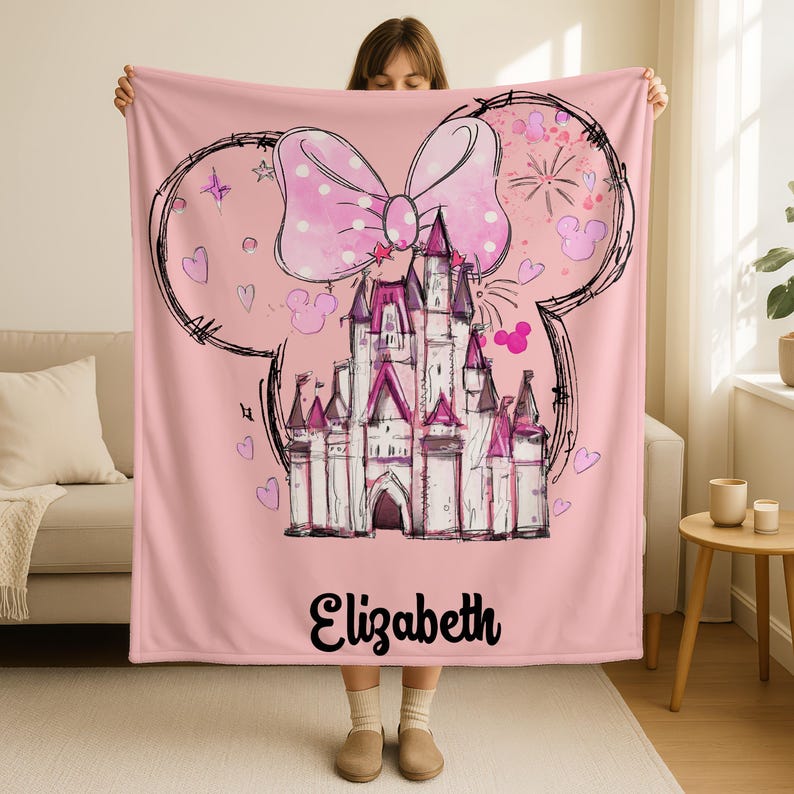 A woman is holding up a pink blanket with a castle and a bow on it.