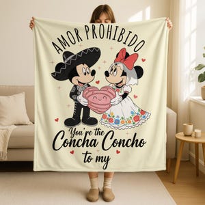 A woman is holding up a blanket with a cartoon image of Mickey Mouse and Minnie Mouse, along with the text "Amor Prohibido" and "You're the Concha Concho to my".