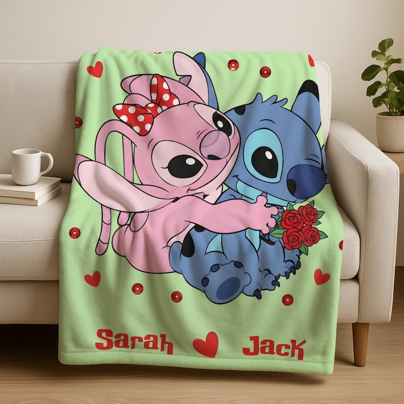 A green blanket with a cartoon image of two characters, a pink bunny and a blue cat, sitting together and holding a bouquet of flowers. The blanket has the names 'Sarah' and 'Jack' printed on it.