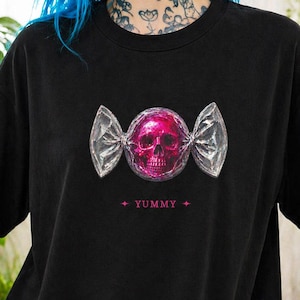 May include: Black t-shirt featuring a pink skull candy graphic. The skull is wrapped in a silver foil design, with the word "YUMMY" printed below. The shirt is a casual, oversized fit.
