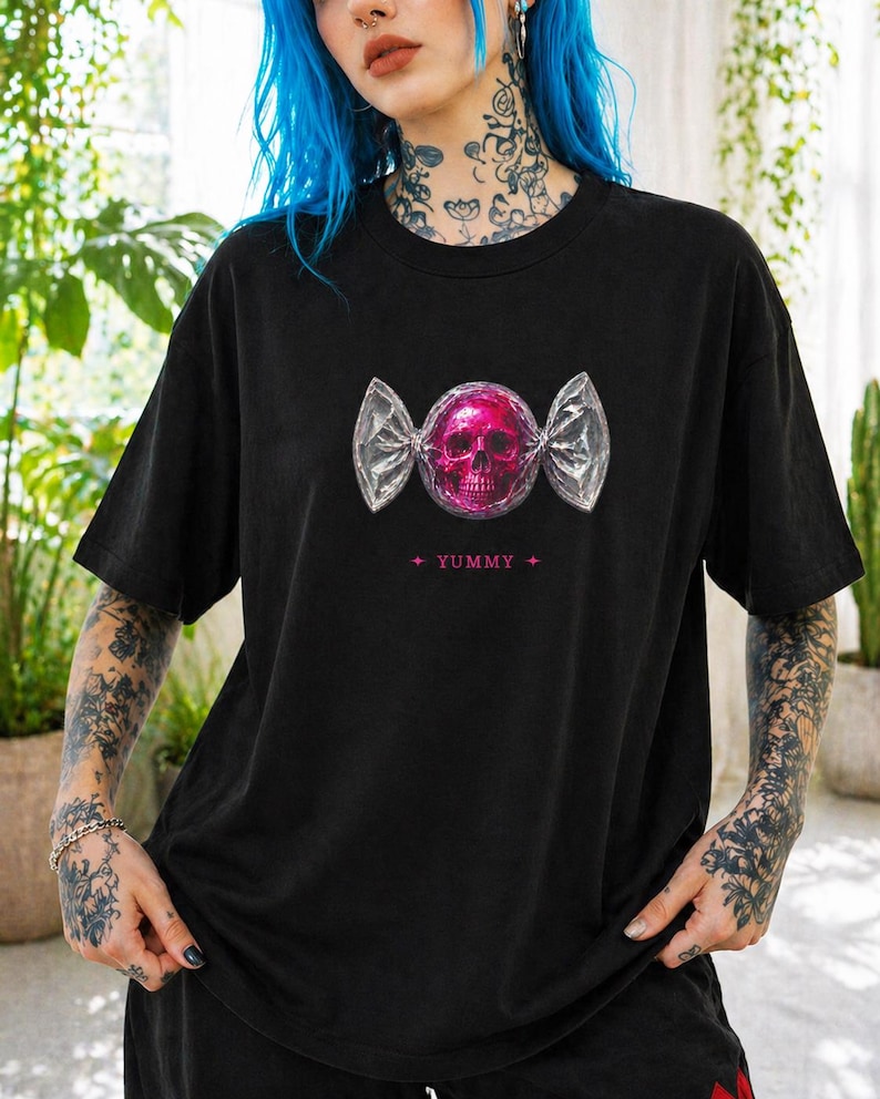 May include: Black t-shirt featuring a pink skull candy graphic. The skull is wrapped in a silver foil design, with the word "YUMMY" printed below. The shirt is a casual, oversized fit.