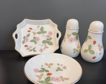 May include: A white porcelain set featuring a square tray with handles, a small round bowl, and two pear-shaped shakers. Each piece is decorated with a botanical pattern of green leaves, pink flowers, and red strawberries, finished with gold trim.