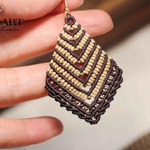Peut inclure: Une paire de boucles d'oreilles nouées brunes et beiges avec des perles dorées. Les boucles d'oreilles ont la forme d'un diamant et présentent un motif géométrique. Les boucles d'oreilles sont faites à la main avec amour.