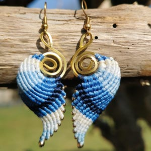 Könnte beinhalten: Ein Paar blaue und weiße Makramee-Ohrringe mit goldenen Metalldraht-Akzenten. Die Ohrringe sind flügelartig geformt.