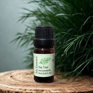 May include: A small amber glass bottle of 5th Essence Tea Tree Pure Essential Oil. The label features a green sprig illustration and the text "Tea Tree Pure Essential Oil 10 mL (0.33 FL. OZ.)". The bottle has a black cap.