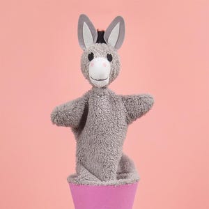 May include: A gray plush donkey puppet with black ears and a pink nose, standing in a pink cone-shaped base.