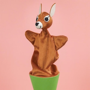 May include: A brown kangaroo hand puppet with a white and black face, white ears, and outstretched arms. The puppet is set against a pink background and is attached to a green cylinder base.