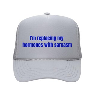Puede incluir: Una gorra de camionero gris con un mensaje bordado en azul que dice "Estoy reemplazando mis hormonas por sarcasmo".