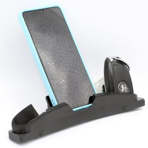 May include: A black car phone holder with a light blue phone and a black key fob with a silver key ring.