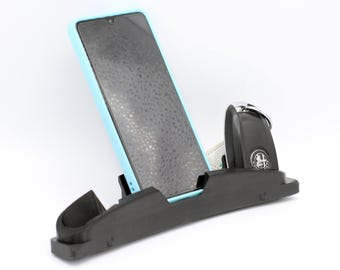Könnte beinhalten: Ein schwarzer Auto-Telefonhalter mit einem hellblauen Telefon und einem schwarzen Schlüsselanhänger mit einem silbernen Schlüsselring.