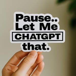 May include: A white sticker with black text that reads "Pause.. Let Me CHATGPT that." The text is in a bold, sans-serif font. The sticker is held by a hand against a neutral background.