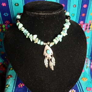 Puede incluir: Un collar de cuentas turquesa y negras con un colgante de plata con una piedra turquesa y tres plumas.
