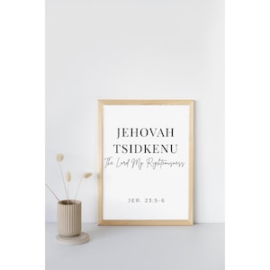 May include: A framed print with the words "JEHOVAH TSIDKENU The Lord My Righteousness" in black font. The print is in a light wood frame. A beige vase with dried flowers sits to the left of the print.