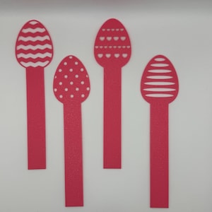 Può includere: Quattro ritagli rossi a forma di uovo di Pasqua con motivi decorativi. I motivi includono linee orizzontali, pois e forme di cuore. Ogni ritaglio ha uno stelo rettangolare e sono disposti su uno sfondo bianco.