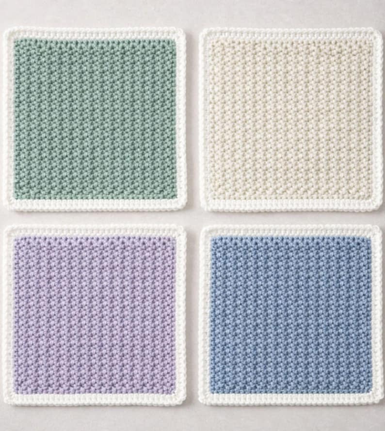 May include: A set of four square crochet coasters featuring a textured stitch pattern. Each coaster has a solid colored center in sage green, cream, lavender, or dusty blue, and is finished with a clean white border around the entire perimeter.