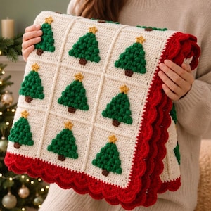 May include: A cream-colored crochet blanket featuring a grid pattern of textured green Christmas trees with brown trunks and yellow star toppers. The blanket is finished with a wide, scalloped red border along the edges, creating a festive design.