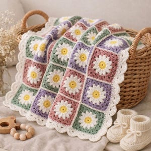 May include: A handmade crochet baby blanket with daisy flower squares in pastel colors of pink, green, and purple. The blanket is placed in a wicker basket with a pair of white knitted baby booties.
