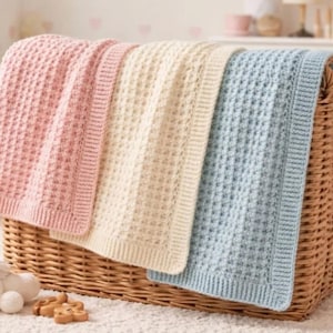 Puede incluir: Tres mantas de bebé de colores pastel con un diseño texturizado, en una cesta de mimbre. Las mantas son rosa, crema y azul claro. Tienen un patrón de gofres y están dobladas sobre el borde de la cesta.