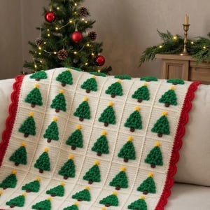 May include: A cream-colored crocheted blanket featuring a repeating grid pattern of small, textured green Christmas trees with brown trunks and yellow star toppers. The blanket is finished with a scalloped red border along the edges.