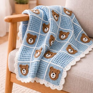 May include: A light blue crochet baby blanket with a repeating pattern of brown teddy bear faces. The blanket has a waffle-like texture and a white scalloped edge. The blanket is draped over a wooden chair.