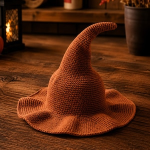 May include: A burnt orange crochet hat featuring a wide, wavy brim and a tall, pointed crown that curves slightly at the top. The hat is constructed with a dense, uniform stitch pattern throughout, creating a textured surface in a solid colour.