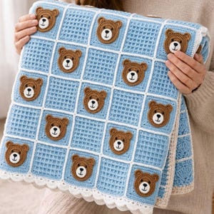 May include: A light blue crochet blanket featuring a grid pattern of white lines and brown teddy bear faces. The blanket has a textured waffle stitch design and a scalloped white border along the bottom edge, creating a repeating pattern of bears.