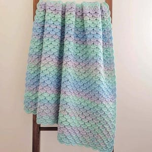 May include: A crochet blanket featuring a repeating scalloped shell pattern in a gradient of soft pastel colors including light blue, mint green, and lavender. The textile has a textured, layered appearance created by the interlocking yarn stitches.