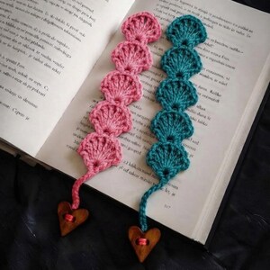 May include: Two handmade crochet bookmarks, one in pink and one in teal, featuring a repeating scalloped shell pattern. Each bookmark ends with a thin yarn tail attached to a small, smooth, brown wooden heart-shaped bead with a center hole.