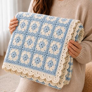 May include: A handmade crochet blanket featuring a repeating square pattern of light blue and cream-coloured yarn. The design consists of floral-inspired motifs within each square, finished with a decorative scalloped edge in cream yarn.