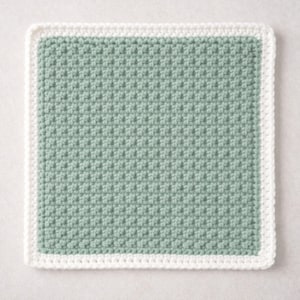 May include: A square crochet coaster featuring a textured sage green center panel with a consistent, repeating stitch pattern. The square is framed by a solid white border made of a smooth, uniform crochet stitch that outlines the entire perimeter.