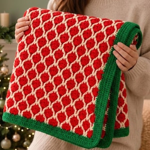 May include: A crocheted blanket featuring a repeating red and cream lattice pattern. The blanket is finished with a solid dark green border along the edges, showcasing a textured yarn construction with a consistent geometric design throughout.