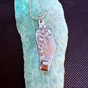 May include: A silver pendant necklace featuring a floral design. The pendant is crafted from a repurposed spoon, showcasing intricate flower details. The necklace has a delicate silver chain, perfect for everyday wear.