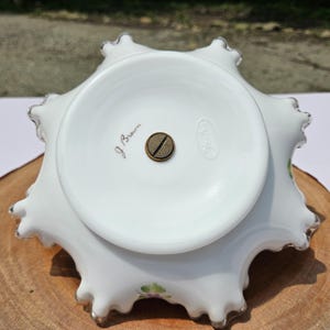 Puede incluir: Cuenco de cristal Fenton blanco con borde ondulado y borde plateado. La base tiene una base circular con un tornillo de lat&oacute;n y el texto "J. Brown" y "Fenton". El cuenco tiene un dise&ntilde;o floral.
