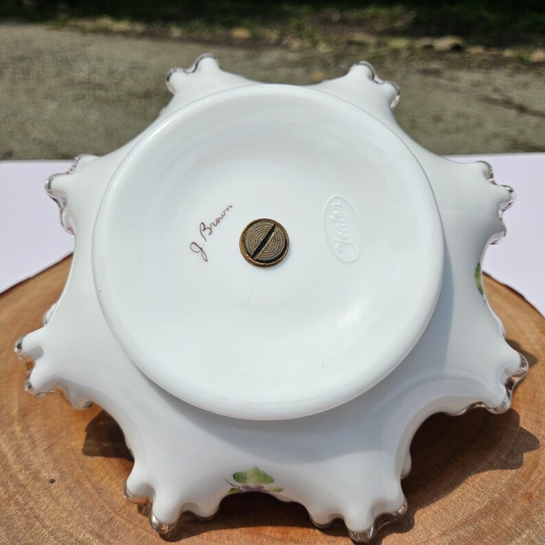 Puede incluir: Cuenco de cristal Fenton blanco con borde ondulado y borde plateado. La base tiene una base circular con un tornillo de lat&oacute;n y el texto "J. Brown" y "Fenton". El cuenco tiene un dise&ntilde;o floral.