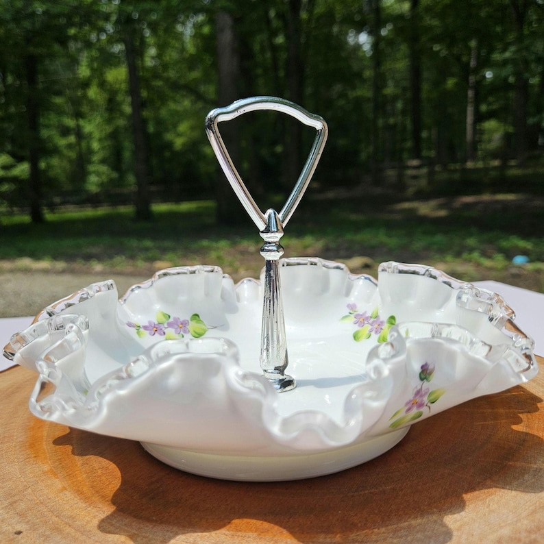 Puede incluir: Una fuente blanca de dos niveles con borde ondulado y asa plateada. La fuente presenta delicados detalles florales morados y un ribete plateado. Dise&ntilde;ada para exhibir y servir alimentos.