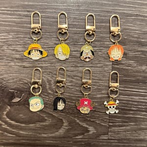 Puede incluir: Ocho llaveros dorados con diferentes personajes de dibujos animados del anime One Piece. Los personajes incluyen a Luffy, Zoro, Nami, Sanji, Chopper, Usopp, Franky y Brook.